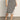 A woman wears the Sanctuary Clothing side slit midi black macrame stripe 2 skirt with a matching top and black sandals, standing on a gray floor against a plain light background.