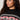 A person with long curly hair wears the "send it sweater black multi extended sizing" by Sanctuary Clothing, featuring a red and white geometric chest pattern. They look off to the side with a neutral expression.