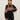 A woman models the Sanctuary Clothing "send it sweater black multi"€�a black knit with red, white, and pink geometric patterns€�and a matching beanie, posing confidently against a plain background.