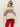 A woman wears the Sanctuary Clothing send it sweater chalk multi€�cream-colored with red and black geometric patterns€�with bright red pants and sunglasses, standing against a plain light background.