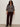 A woman stands against a plain light background wearing Sanctuary Clothing's zip up fairisle hoodie in mocha fairisle extended sizing, paired with sunglasses, burgundy corduroy pants, and black ankle boots.