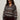 A woman with curly hair wears sunglasses, gold hoop earrings, and the Sanctuary Clothing zip up fairisle hoodie mocha fairisle extended sizing, styled with dark pants against a plain light background.