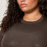 A woman with curly dark hair wears the Sanctuary Clothing Sparkle Sequin Sweater Ink (extended sizing), shown from the shoulders up against a light background.