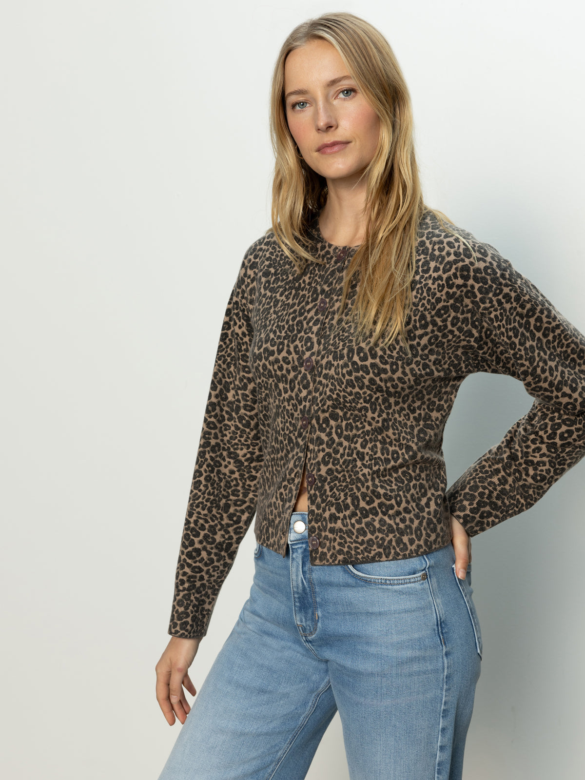 A woman with long blonde hair wears the Sanctuary Clothing must have cardi french kitty, standing against a plain light background with one hand on her hip, gazing confidently at the camera.