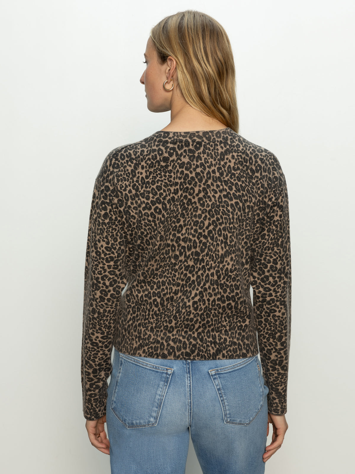 A woman with long, straight blonde hair is seen from the back wearing Sanctuary Clothing’s must have cardi french kitty sweater in brown and black leopard print, paired with light blue jeans against a plain white background.