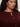 A person with curly dark hair wears the Sanctuary Clothing boucle cardi in dark crimson (extended sizing), featuring three brown buttons, a round neckline with a notch, and small gold hoop earrings.