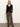A woman with straight blonde hair stands against a plain light wall, wearing the Sanctuary Clothing fitted raglan cardi in black.