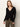 A woman with straight, long blond hair wears the Sanctuary Clothing fitted raglan cardi in black, styled with khaki pants. She stands against a plain light background, facing the camera with a neutral expression.