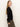 A woman with long, straight blonde hair stands in profile against a plain light background, wearing Sanctuary Clothing's fitted raglan cardi in black and olive green pants, looking slightly over her shoulder.