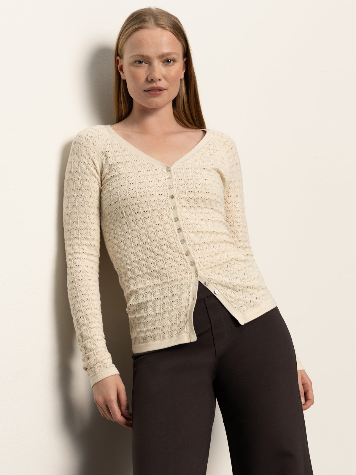 A woman with straight, long blonde hair wears the Sanctuary Clothing fitted raglan cardi in light oat with dark brown pants, standing against a plain light background.