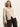 A woman with straight, long blonde hair wears the Sanctuary Clothing fitted raglan cardi in light oat with dark brown pants, standing against a plain light background.