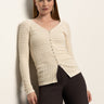 A woman with straight, long blonde hair wears the Sanctuary Clothing fitted raglan cardi in light oat with dark brown pants, standing against a plain light background.
