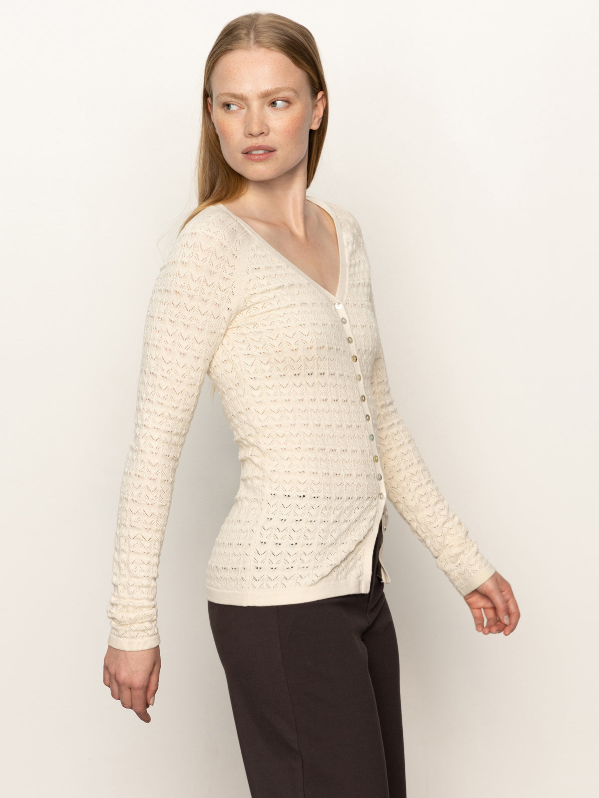A woman with long, straight blonde hair wears the Sanctuary Clothing fitted raglan cardi in light oat and dark pants, standing against a plain light background and looking to her left.