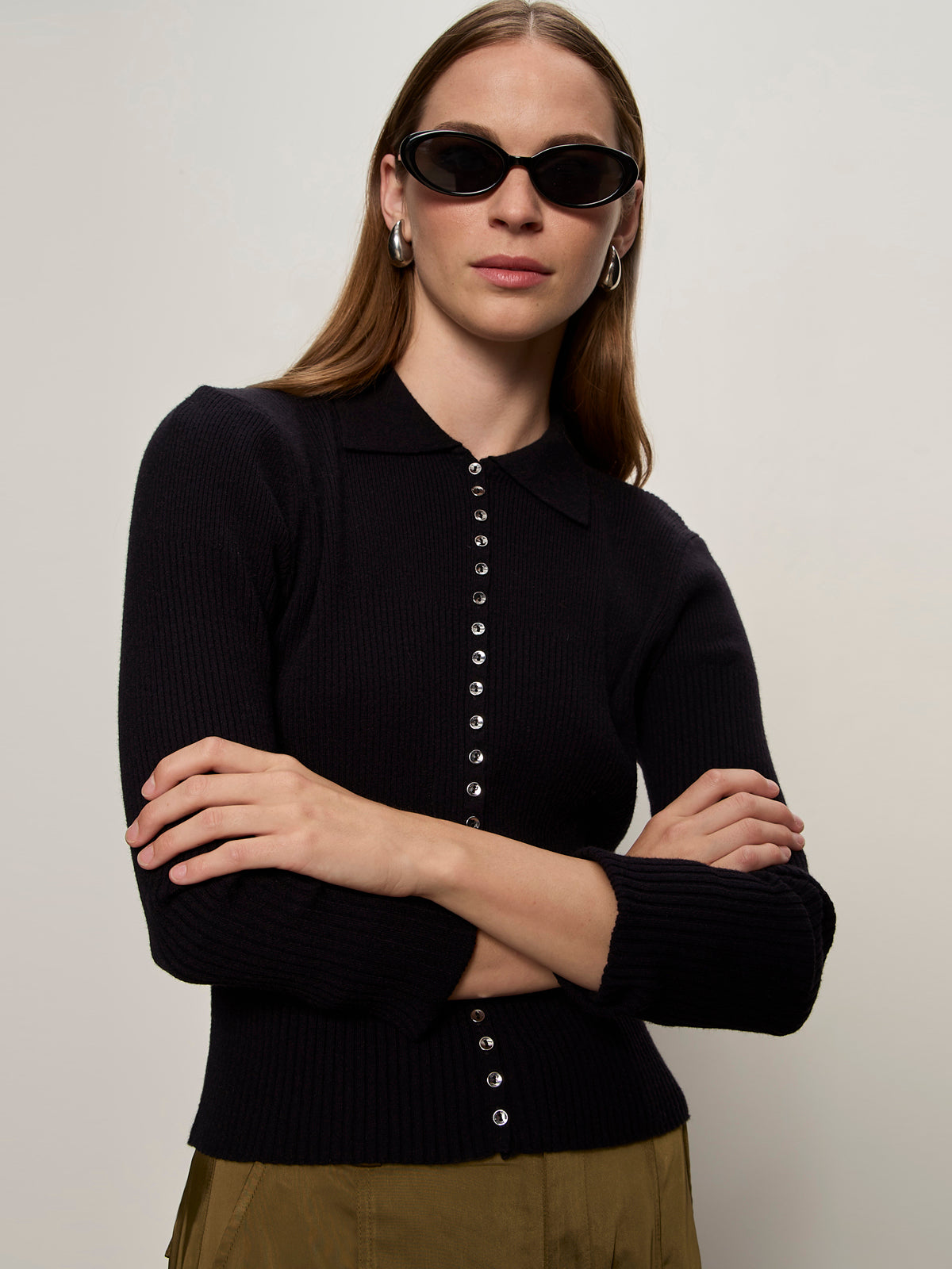 A woman with straight brown hair wears oval black sunglasses, silver hoop earrings, and the Sanctuary Clothing button down variegated cardi in black. She stands with arms crossed against a plain light background.
