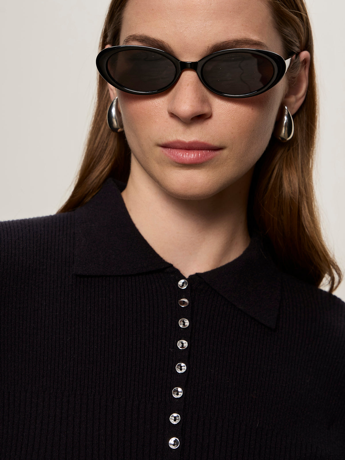 A woman with long brown hair wears black oval sunglasses, large silver hoop earrings, and the Sanctuary Clothing button down variegated cardi in black, confidently looking at the camera against a neutral background.