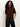 A woman with long, curly hair models the Sanctuary Clothing perfect sweater tee chicory�a short-sleeved, dark brown top�with black leather pants against a light background, hands in her pockets and looking at the camera.