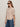 A woman with long brown hair wears dark sunglasses, blue jeans, and the Sanctuary Clothing "perfect sweater tee fawn," standing against a plain light background.