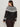 A woman with long brown hair, dressed in Sanctuary Clothing’s fairisle crewneck cardi ink multi extended sizing and dark brown pants, stands facing away and looks over her left shoulder.