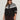 A woman wearing Sanctuary Clothing’s fairisle crewneck cardi ink multi (extended sizing), featuring white and black Fair Isle patterns, stands confidently against a light background, sunglasses on and hands by her sides.