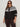 A woman wearing Sanctuary Clothing’s fairisle crewneck cardi ink multi (extended sizing), featuring white and black Fair Isle patterns, stands confidently against a light background, sunglasses on and hands by her sides.