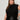 A woman with long brown hair models the Sanctuary Clothing city sweater shell black (extended sizing), paired with a black leather skirt. She stands against a light background, looking confidently at the camera with one hand on her hip.