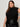 A woman with long brown hair models the Sanctuary Clothing city sweater shell black (extended sizing), paired with a black leather skirt. She stands against a light background, looking confidently at the camera with one hand on her hip.