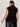 A woman with long brown hair is seen from the back wearing the Sanctuary Clothing city sweater shell in black (extended sizing) and a black leather skirt, standing against a light background.