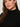 A woman with long brown hair wearing the city sweater shell in black by Sanctuary Clothing looks at the camera with a neutral expression. The image is cropped to show her from the shoulders up.