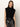 A woman with wavy brown hair wears the Sanctuary Clothing city sweater shell in black, paired with high-waisted black leather pants, standing against a light background and looking at the camera with a neutral expression.