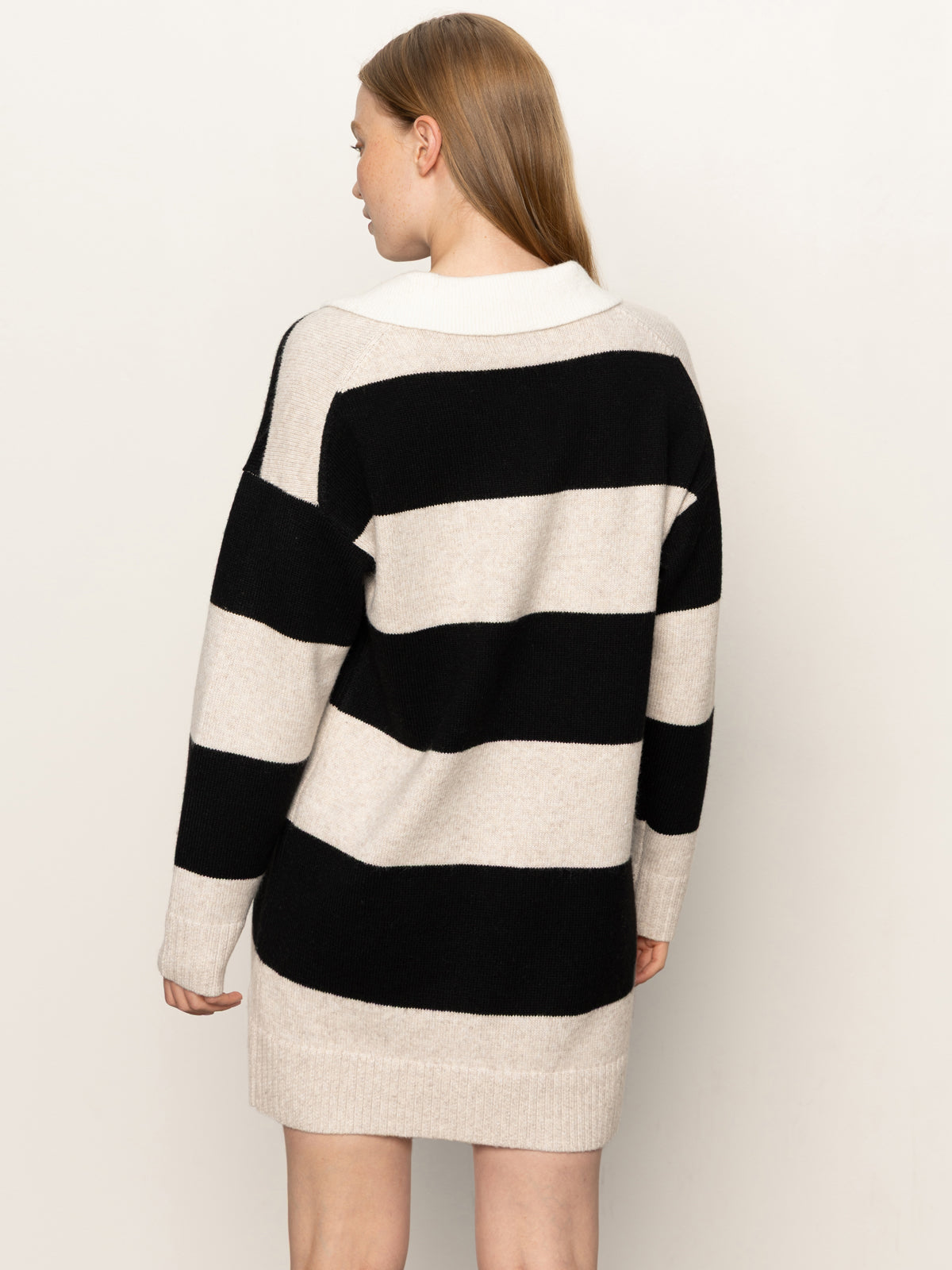 A person with straight, light brown hair is shown from the back wearing Sanctuary Clothing's polo striped sweater dress in heather pearl with black, featuring wide horizontal stripes, against a plain light background.