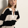 A woman with straight blonde hair models the Sanctuary Clothing polo striped sweater dress in heather pearl with black, featuring a white collar. She stands against a light background, looking slightly aside with a neutral expression.