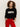 A woman with curly hair wears the Sanctuary Clothing "life of the party" cashmere sweater in black with chalk lettering, paired with bright red pants, standing against a plain light background with her hands in her pockets.