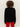 A person with curly brown hair is seen from behind wearing the Sanctuary Clothing life of the party cashmere sweater in black with chalk, paired with red pants, against a plain, light background.