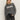 A woman with long blonde hair wears the Sanctuary Clothing "life of the party" cashmere sweater in heather charcoal with chalk lettering, styled with dark jeans and a black belt, standing against a plain light background.