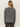 A person with long, straight blonde hair wears the Sanctuary Clothing life of the party cashmere sweater in heather charcoal with chalk, paired with dark jeans, standing with their back to the camera against a plain light background.