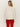 A woman with straight blonde hair and large hoop earrings wears the Sanctuary Clothing 24 7 Popover in chalk with black. She stands facing away against a light background, showing off her long-sleeve sweater and bright red pants.