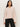 A woman with long dark hair wears the Sanctuary Clothing dreamy v neck sweater in heather rose and black pants, standing against a light background with a neutral expression, facing forward.