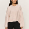 A woman with long dark hair wears the Sanctuary Clothing dreamy v neck sweater in heather rose and black pants, standing against a light background with a neutral expression, facing forward.