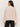 A woman with long dark hair and gold hoop earrings wears the Sanctuary Clothing dreamy v neck sweater in heather rose, paired with black pants, standing facing away from the camera against a plain light background.