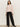 A woman with long dark hair and a neutral expression wears the Sanctuary Clothing dreamy v neck sweater in heather rose, paired with black wide-leg pants and black heeled boots, standing against a plain light background with arms relaxed at her sides.