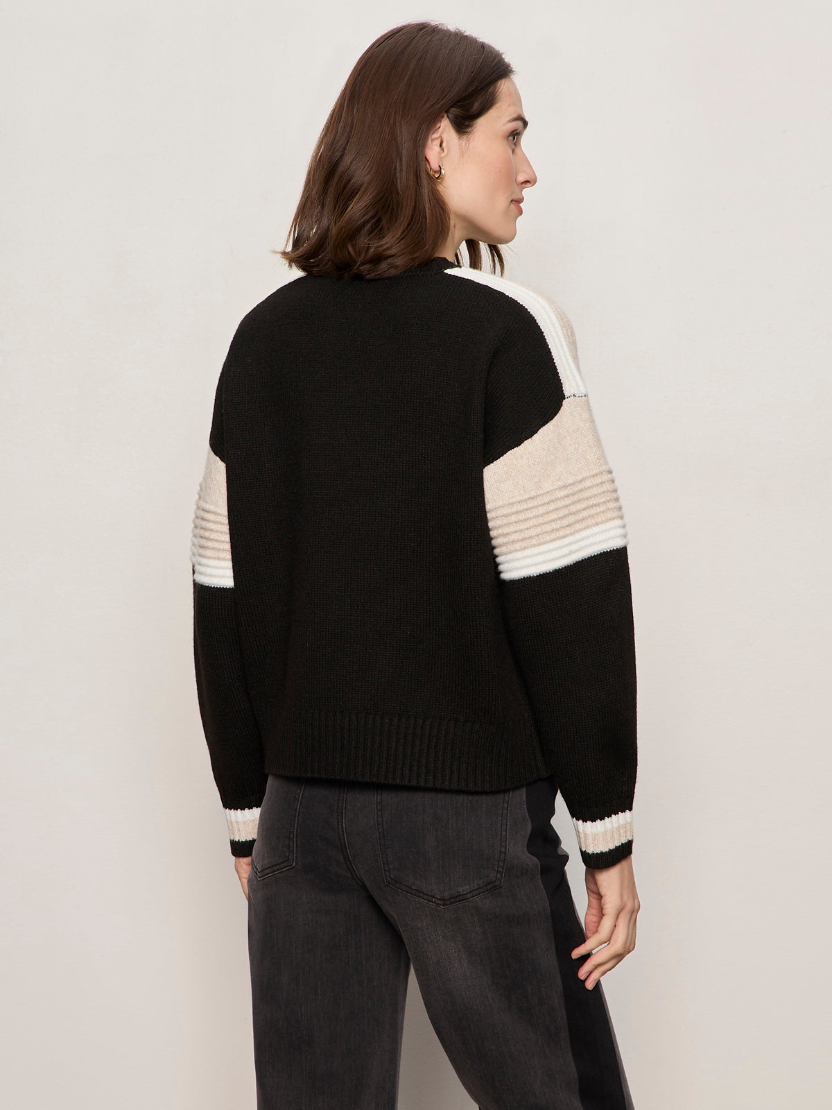 A woman with shoulder-length brown hair, seen from behind in dark jeans, models the Sanctuary Clothing sporty stripe crewneck sweater in black multi against a plain light background.