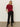 A woman with straight blonde hair poses against a plain background in the Sanctuary Clothing short sleeve shine sweater tee in cherry lacquer shine, paired with black wide-leg pants with button-hem details and black ankle boots.