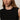 A woman with long brown hair wears the Sanctuary Clothing shine sweater shell in black with black shine, a sleeveless textured top featuring subtle sparkly stripes. She accessorizes with gold hoop earrings and faces the camera neutrally.