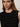 A woman with long brown hair wears the Sanctuary Clothing shine sweater shell in black with black shine, a sleeveless textured top featuring subtle sparkly stripes. She accessorizes with gold hoop earrings and faces the camera neutrally.