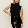 A woman with long blonde hair models the Sanctuary Clothing scarf sweater shell in black, posing with one hand on her hip against a plain light background.