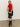 A woman poses against a plain background wearing Sanctuary Clothing„¢s scarf sweater shell in cherry lacquer, paired with a black shiny skirt, black heeled boots, and a small black handbag.