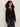 Woman with curly hair wearing the Sanctuary Clothing "must have gem cardi black," featuring small white floral patterns, paired with dark blue jeans and standing against a plain light background.