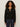 A woman with curly hair wears the Sanctuary Clothing must have gem cardi in black with embroidered florals and dark blue jeans, standing against a plain light background.
