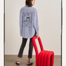 A person wearing the Sanctuary Clothing "the doctor is in shirt blue and white stripe" holds a bold red wavy chair indoors, styled with black jeans and heels.