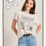 A woman in jeans and a pink "arent gonna keep quiet tee milk" by Sanctuary Clothing, featuring a cartoon print, stands smiling with one hand in her pocket against a white background with cloud doodles.